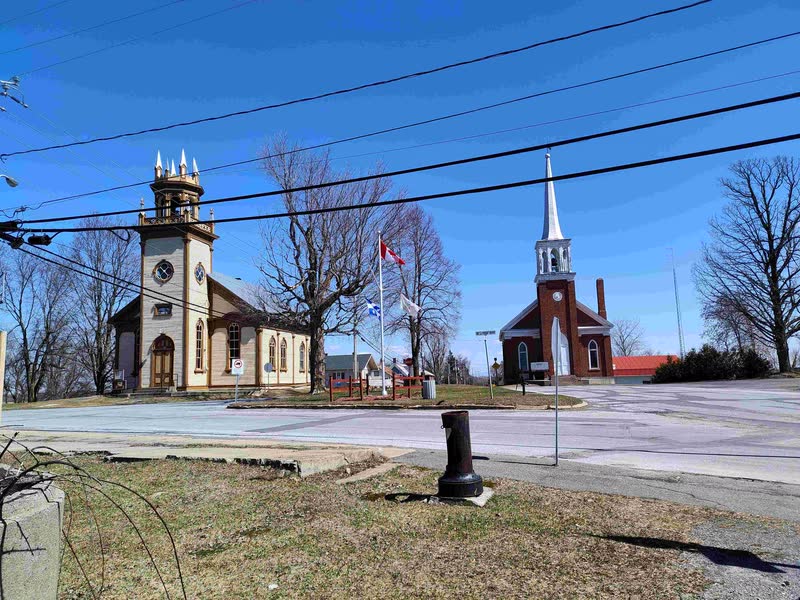 Deux églises, l'une en bois clair, l'autre en brique rouge au clocher blanc, sous un ciel de fin d'hiver